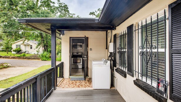 A covered porch with a washing machine and a door leading to a kitchen. - Walkable to FSU Campus: Cozy Retreat w/ Deck! (Tallahassee)