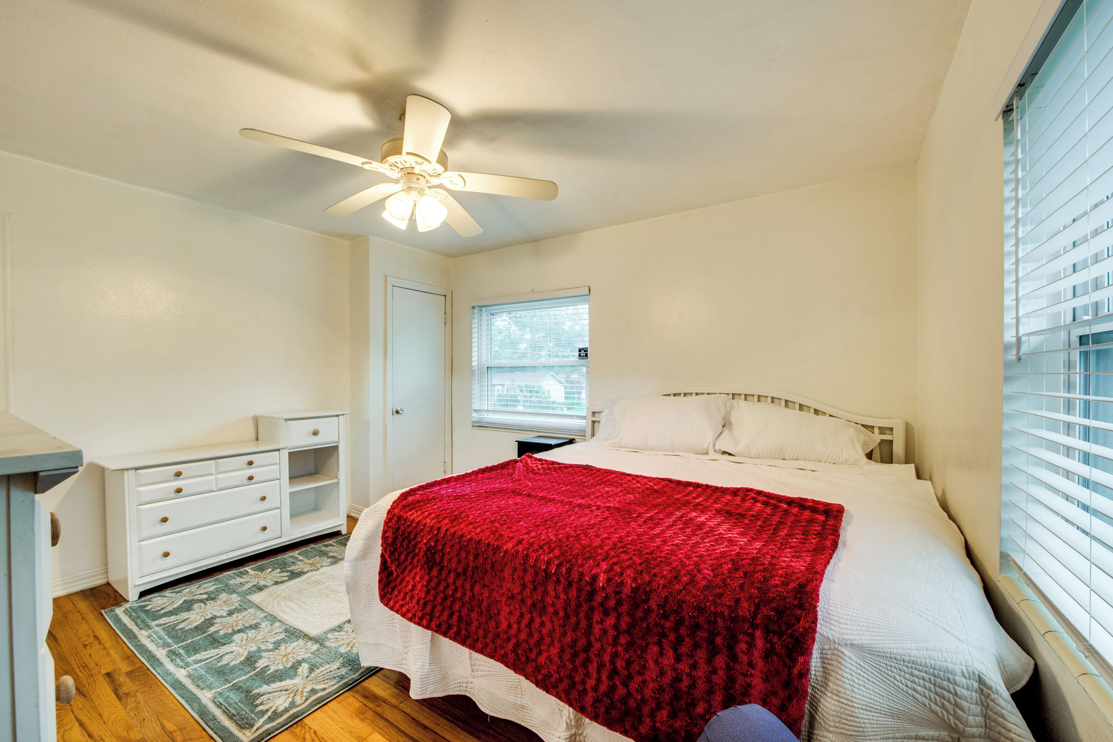 A bedroom with a bed, a white dresser, a ceiling fan, a window, and a door.