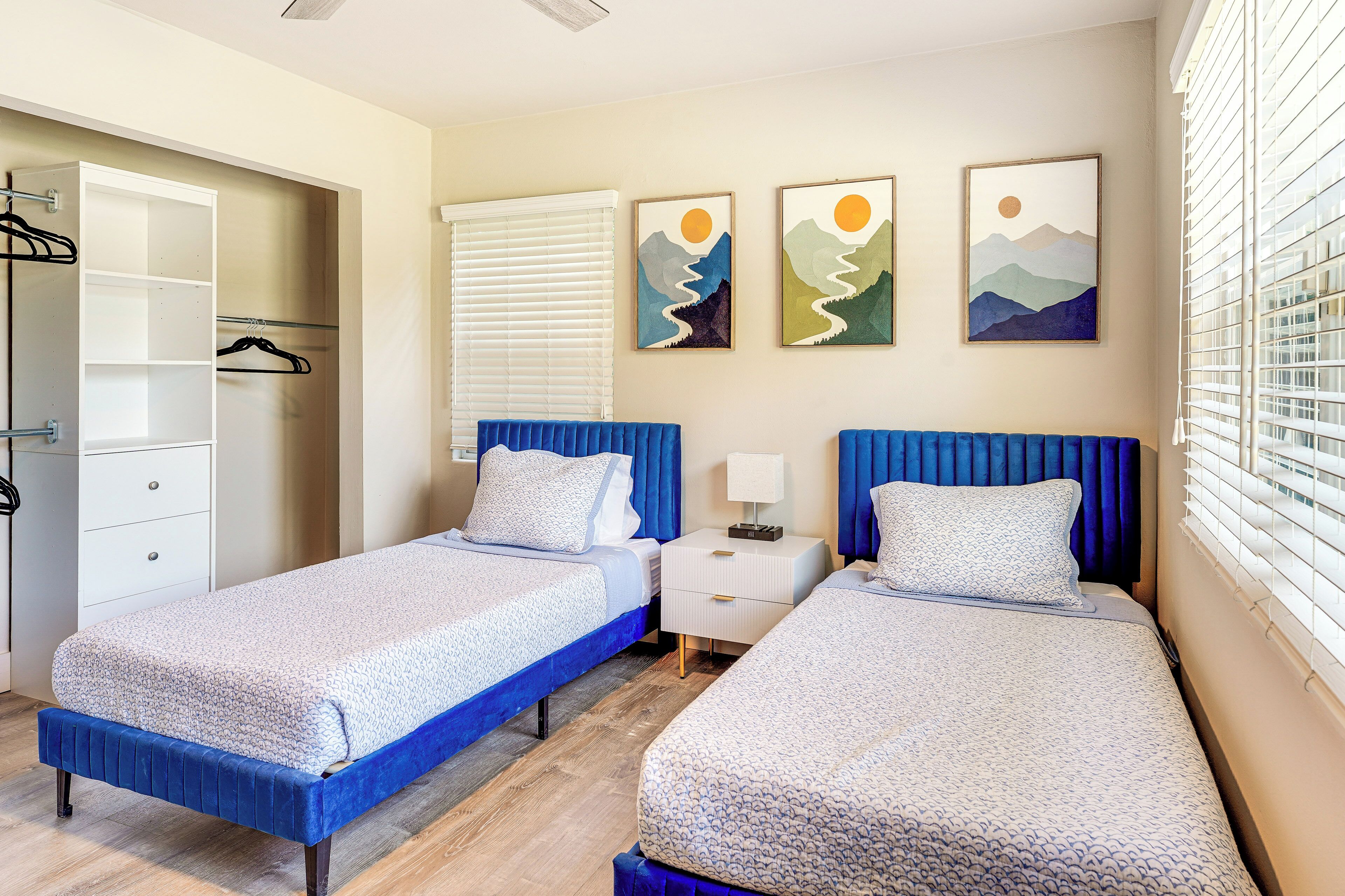 A bedroom with two beds, a wardrobe, and artwork on the wall.