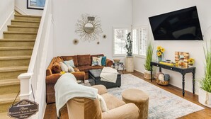 A living room with a staircase, a large mirror, a flat-screen TV, and a sofa. - Walk to Beach: Luxe San Buenaventura Villa! (Port Hueneme)
