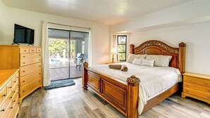 A bedroom with a wooden bed, a television on a dresser, and a sliding glass door leading to a patio.