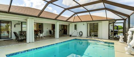 A covered swimming pool with a glass ceiling, adjacent to a room with a tiled floor and a door leading outside.