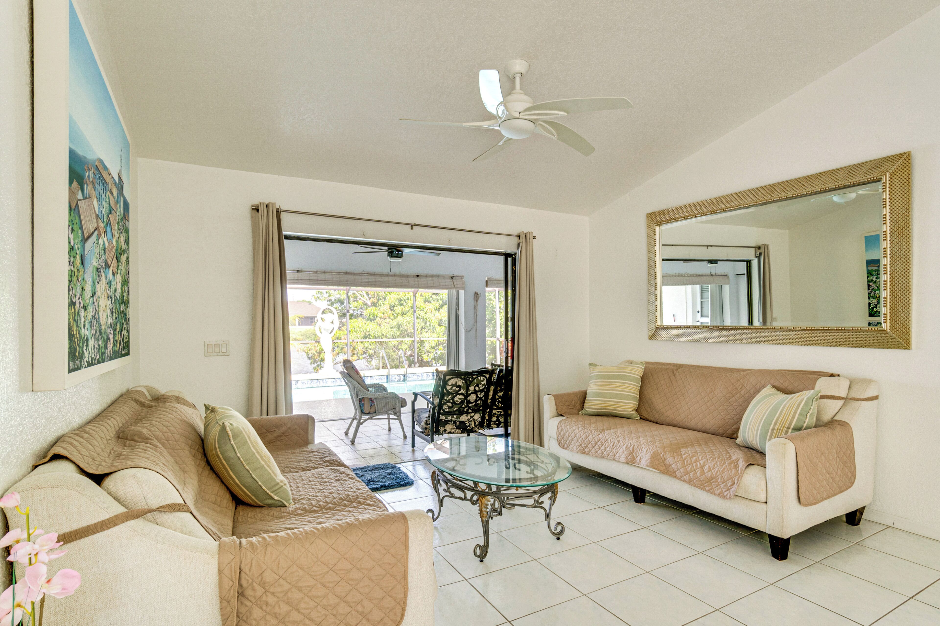 A living room with a glass coffee table, two sofas, a ceiling fan, and a large mirror.