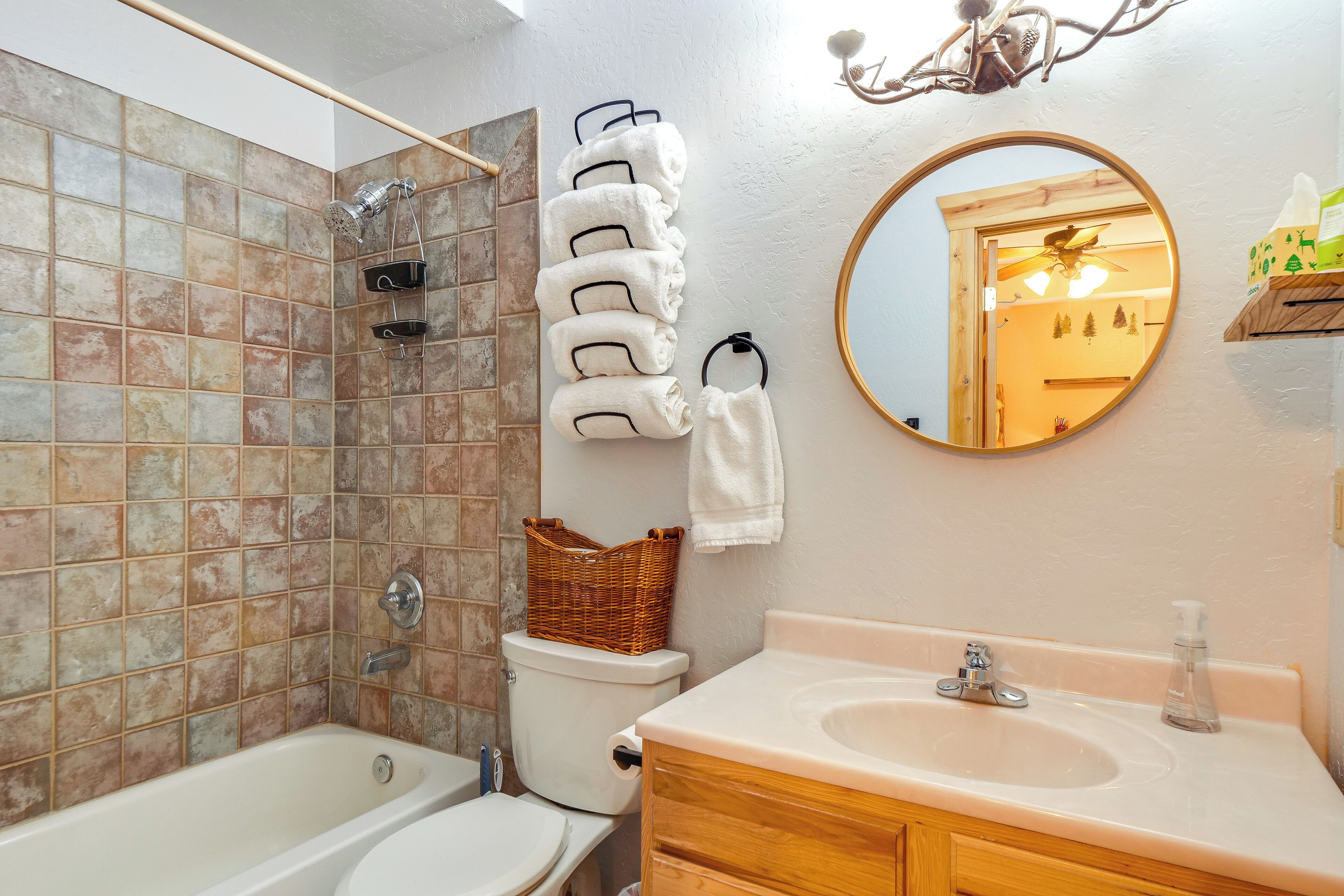 Un baño con bañera, inodoro y lavamanos. Hay un espejo en la pared y un perchero con toallas.