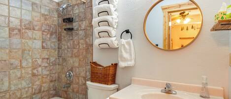 Un baño con bañera, inodoro y lavamanos. Hay un espejo en la pared y un perchero con toallas.