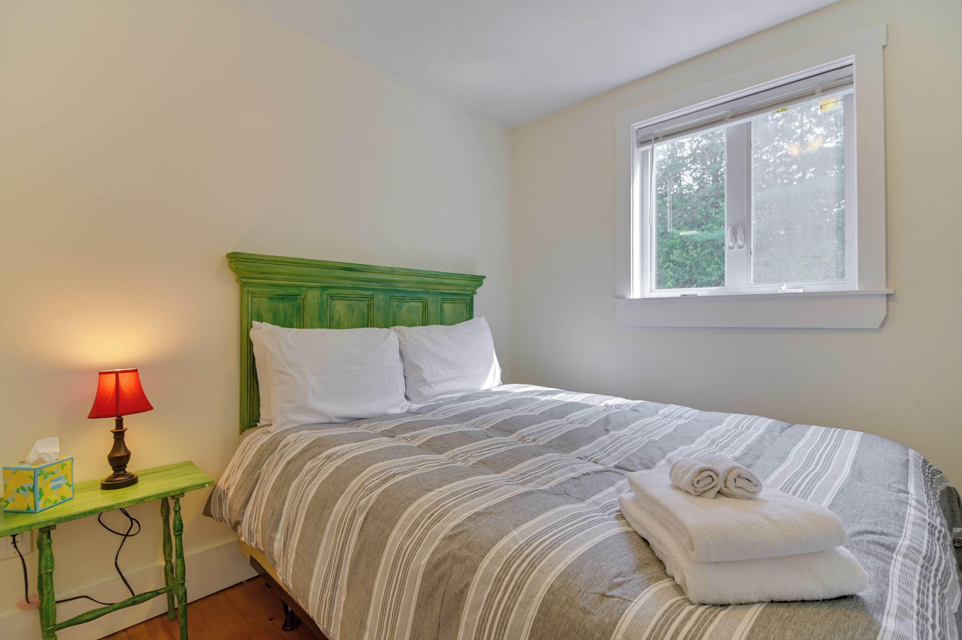 Une chambre à coucher avec une tête de lit verte, une couvre-lit à rayures et une fenêtre donnant sur un paysage verdoyant.