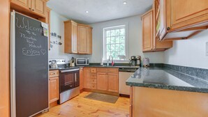 Una cucina con mobili in legno, un frigorifero nero, un forno a microonde e una finestra con vista sugli alberi.