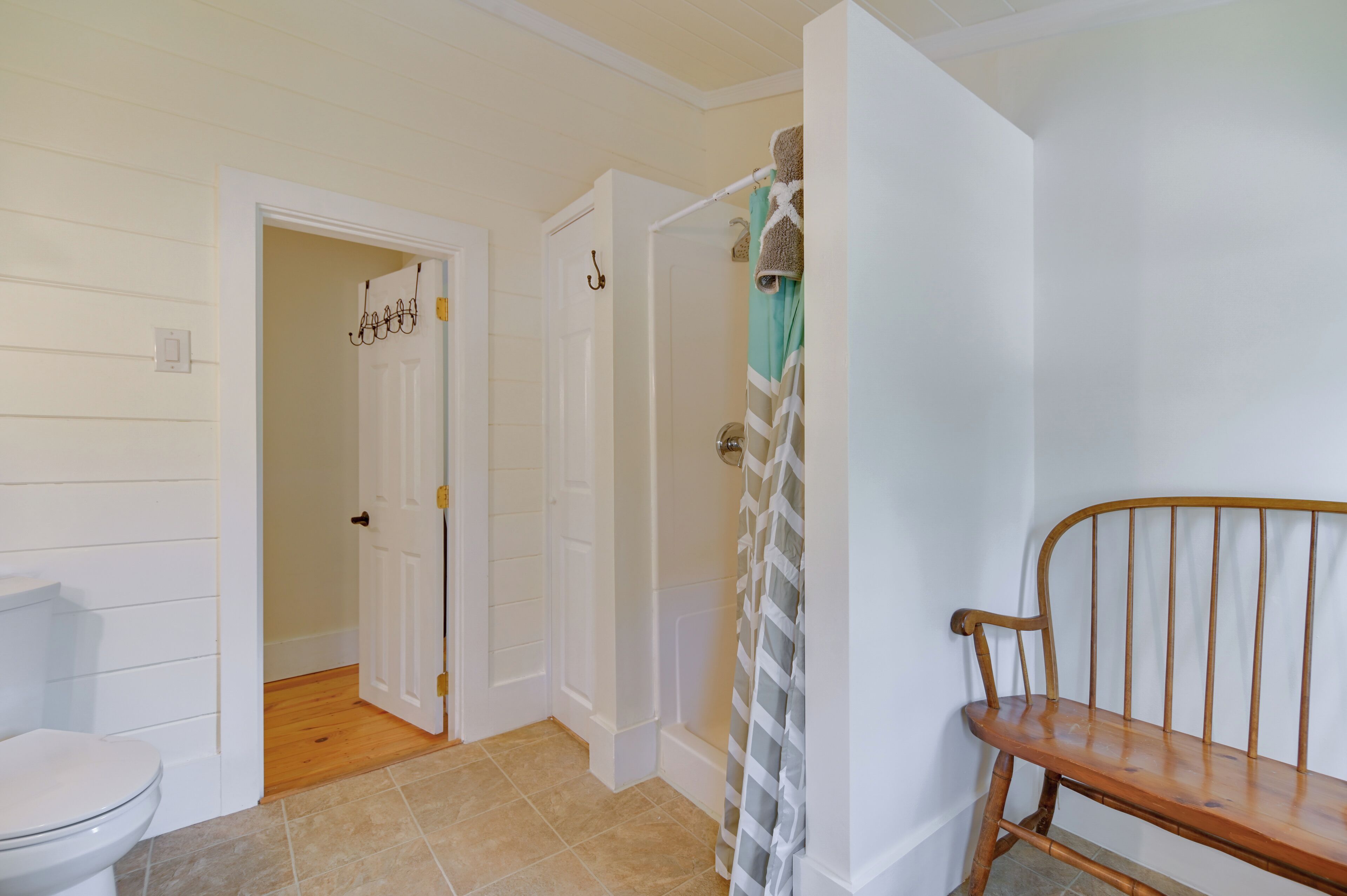 A bathroom with a toilet, a shower, and a wooden bench.