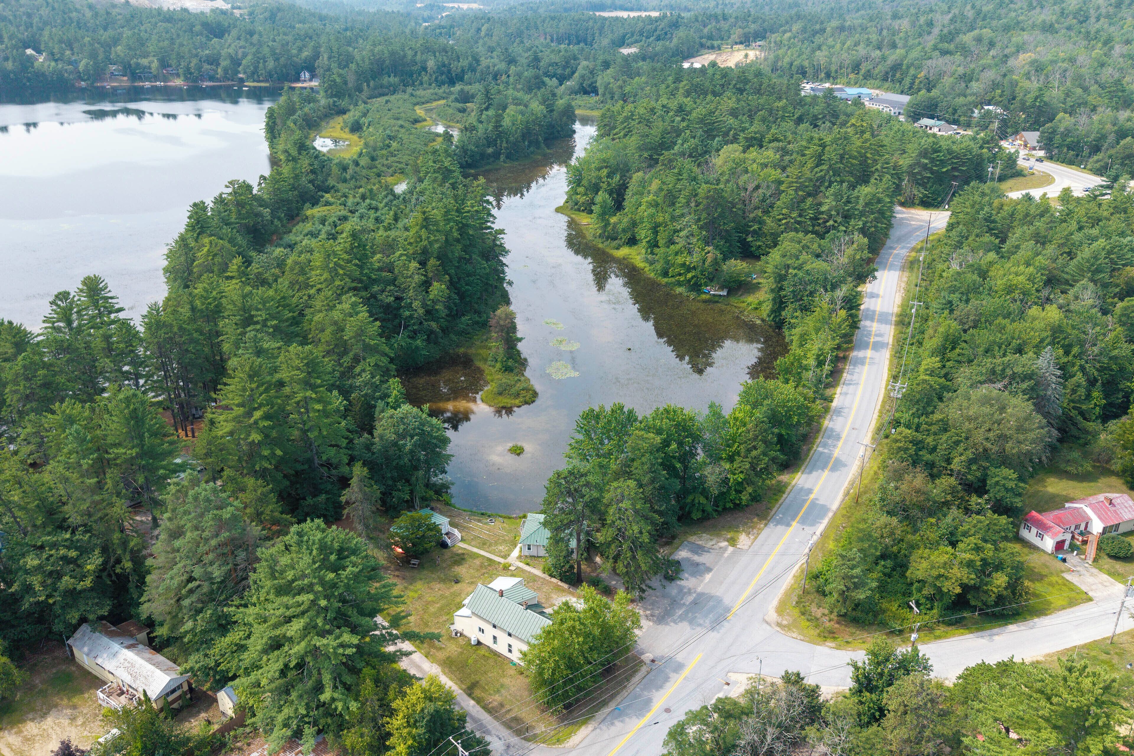 An aerial view of a lakeside property with a road, buildings, and dense forest.