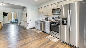 A modern kitchen with stainless steel appliances, wooden flooring, and a staircase leading to another room. - 1 Block to Stroudsburg Main St: Chic Townhome (Stroudsburg)