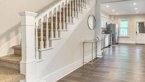 A staircase with white balusters leading to a landing, a kitchen with white cabinets and stainless steel appliances, and a large window providing natural light. - 1 Block to Stroudsburg Main St: Chic Townhome (Stroudsburg)