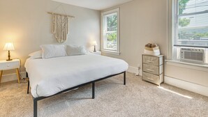 A bedroom with a bed, bedside lamps, a macrame wall hanging, a window with blinds, and a dresser with storage drawers. - 1 Block to Stroudsburg Main St: Chic Townhome (Stroudsburg)