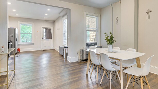 A modern kitchen with white cabinets, a refrigerator, and a dining area with a white table and chairs. - 1 Block to Stroudsburg Main St: Chic Townhome (Stroudsburg)