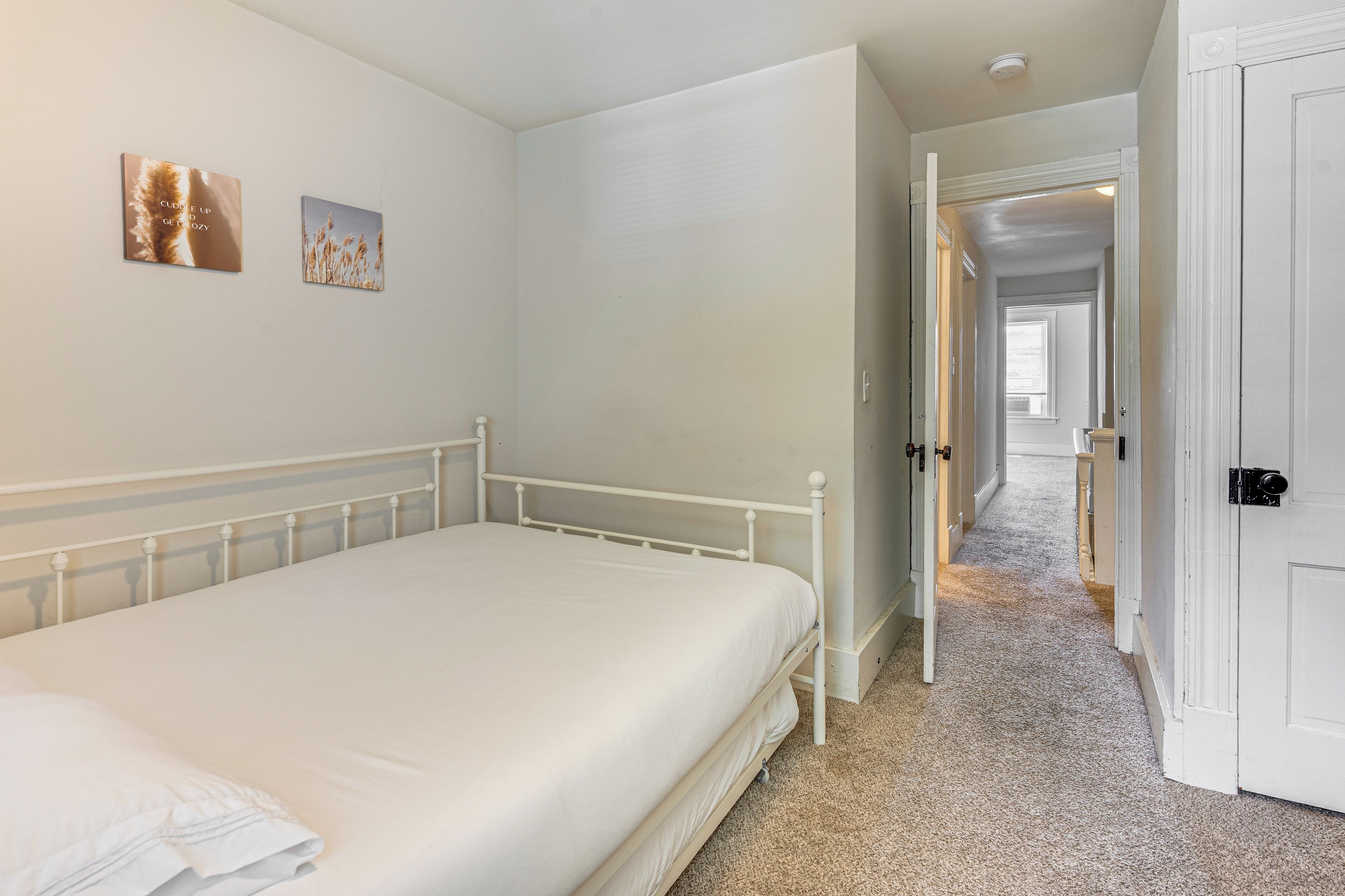 Een slaapkamer met een enkel bed, een deur die naar een gang leidt en twee aan de muur bevestigde foto's.