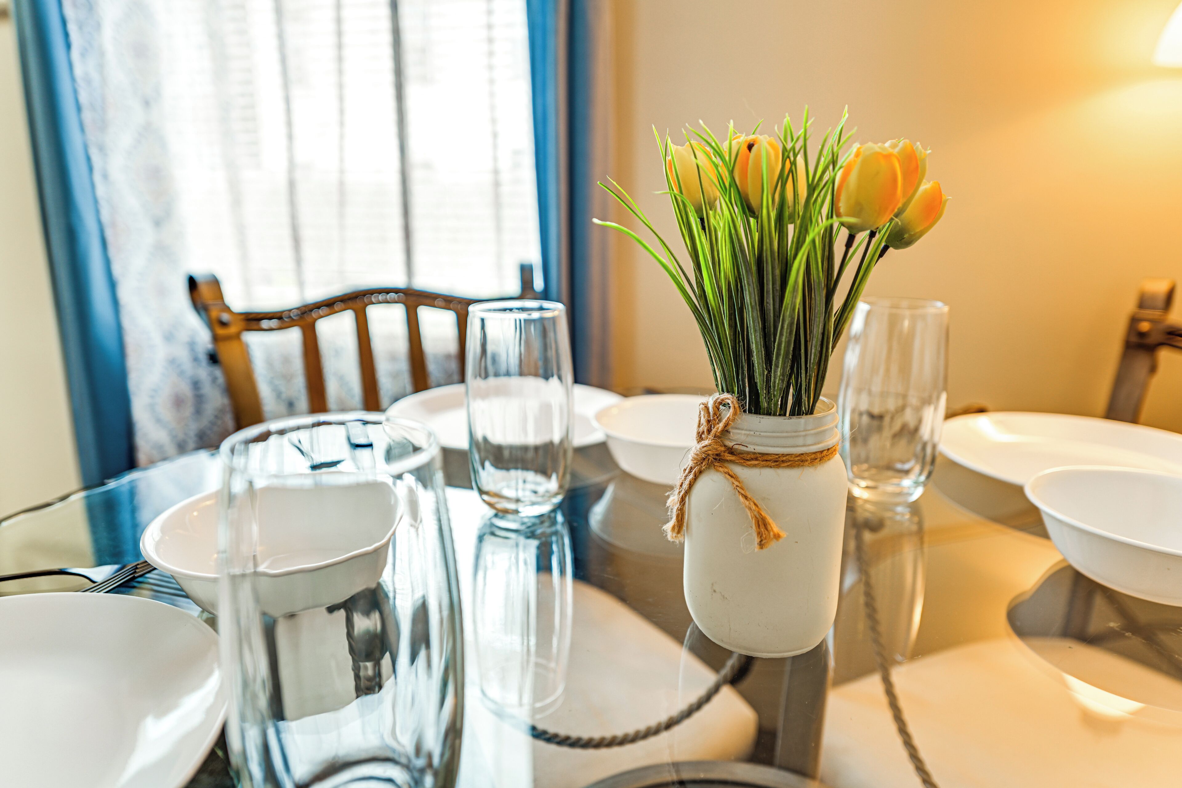 A dining table with a white vase containing yellow tulips, clear glassware, and a wooden chair.