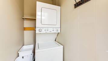 A laundry room with a stacked washer and dryer, a shelf, and a coat rack.