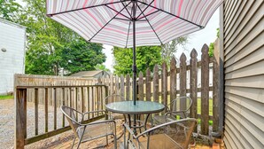 Een terras met een ronde tafel en stoelen, een gestreepte parasol en een houten omheining.