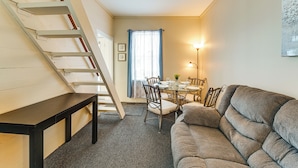 Een gezellige woonkamer met een bank, een eettafel met stoelen, een trap en een raam met gordijnen.