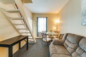 Una sala de estar acogedora con un sofá, una mesa de comedor con sillas, una escalera y una ventana con cortinas.