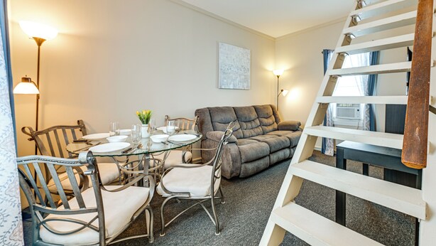 Een eetruimte met een glazen tafel, metalen stoelen en een grijze bank.
