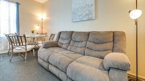 Een knusse woonkamer met een grijze bank, een eettafel met stoelen en een vloerlamp.