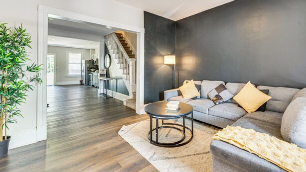Een moderne woonkamer met een grijze bank, een ronde salontafel en een grote potplant.