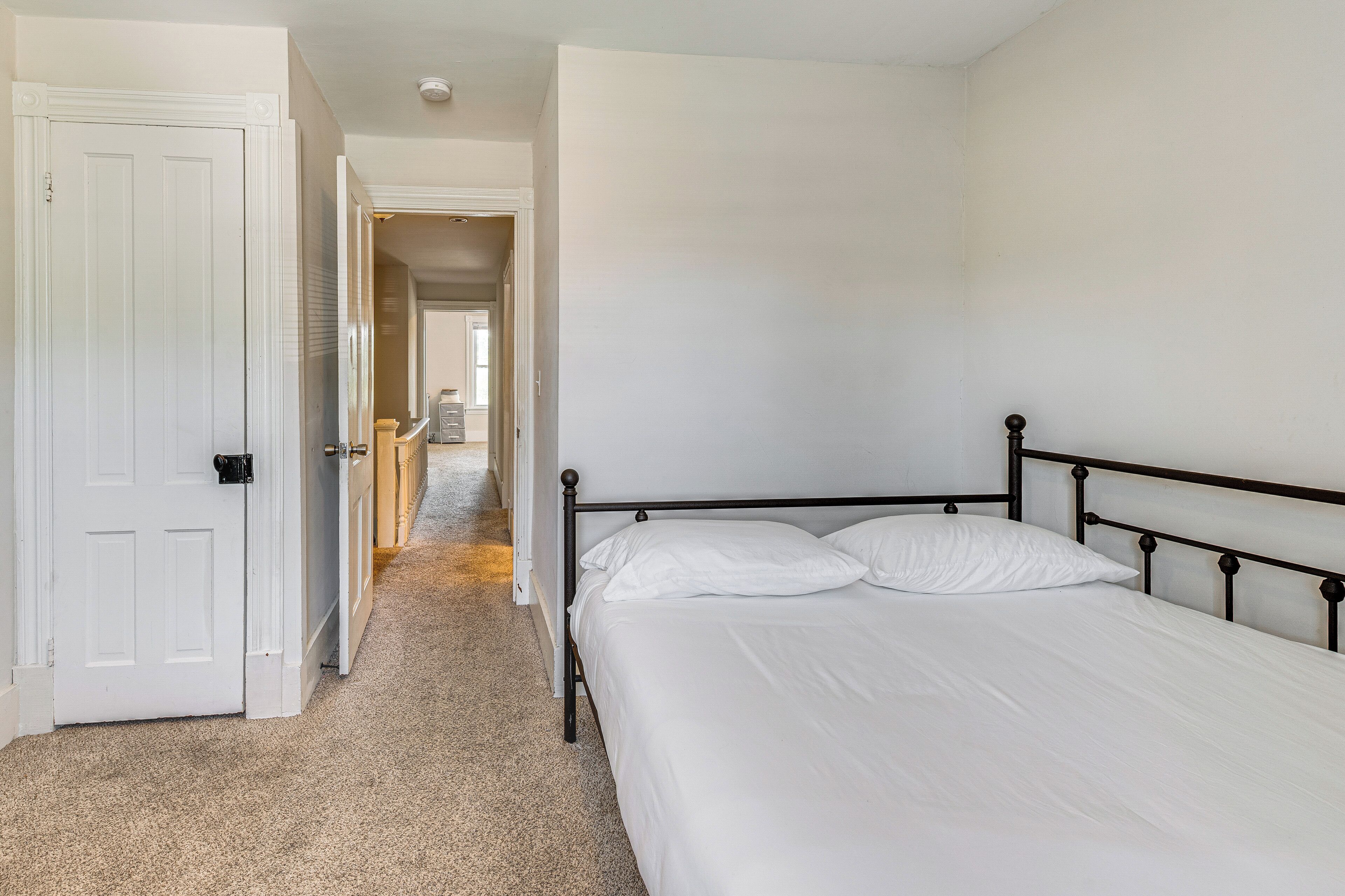 A bedroom with a single bed, a door, and a hallway leading to another room.