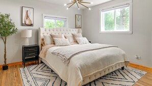 A bedroom with a tufted headboard, a large bed, a bedside table with a lamp, a potted plant, and a geometric rug. - Private Hot Tub, Deck! Group Getaway in Friendship (Friendship)