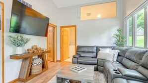 A modern living room with a sectional sofa, a flat-screen TV mounted on the wall, a wooden console table, and a coffee table. - Private Hot Tub, Deck! Group Getaway in Friendship (Friendship)