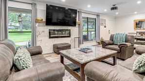 A spacious living room with leather sofas, a marble coffee table, and a flat-screen TV mounted on the wall.