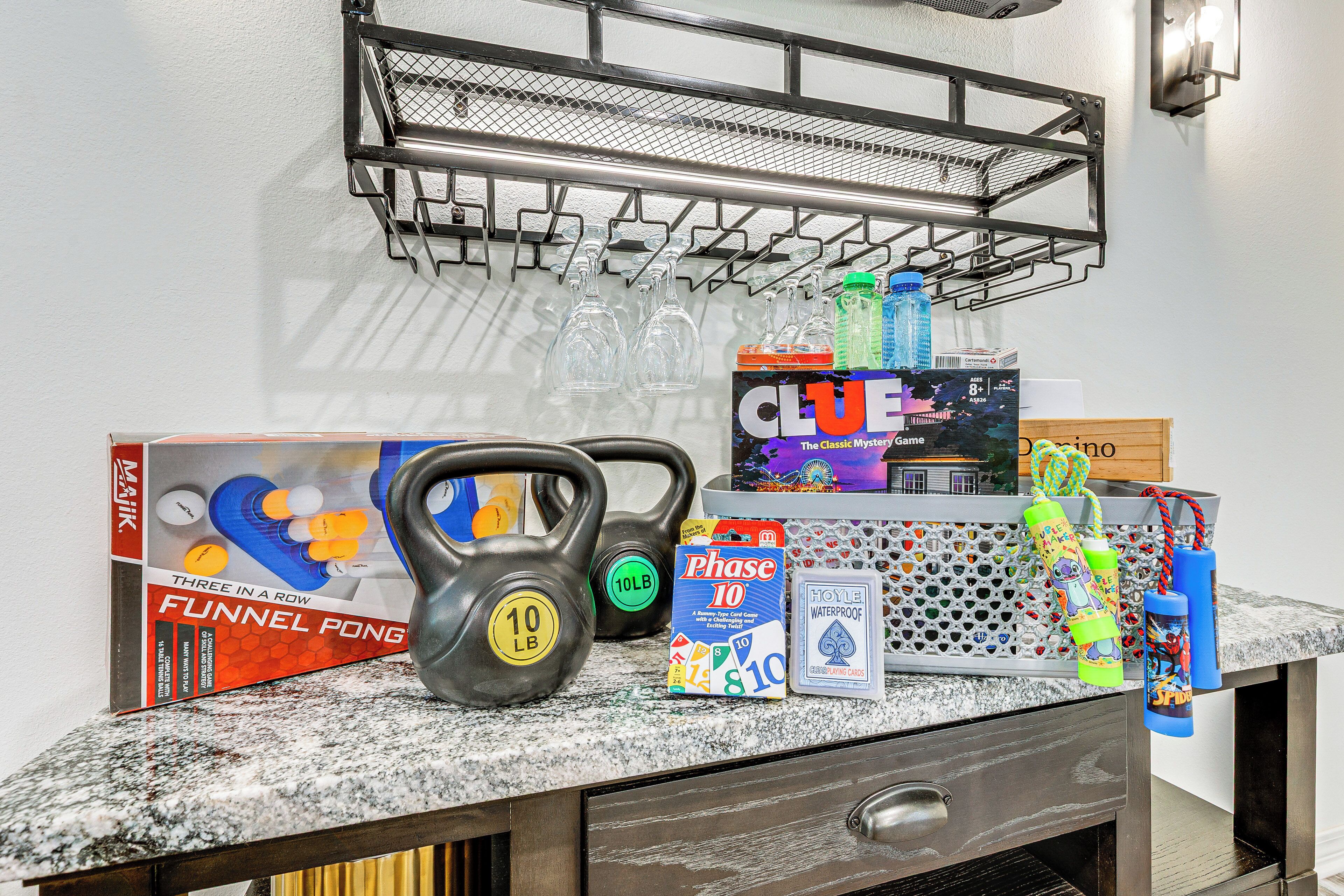 A kitchen counter with various items including kettlebells, a box of funnel pong, a Clue game, and water bottles.