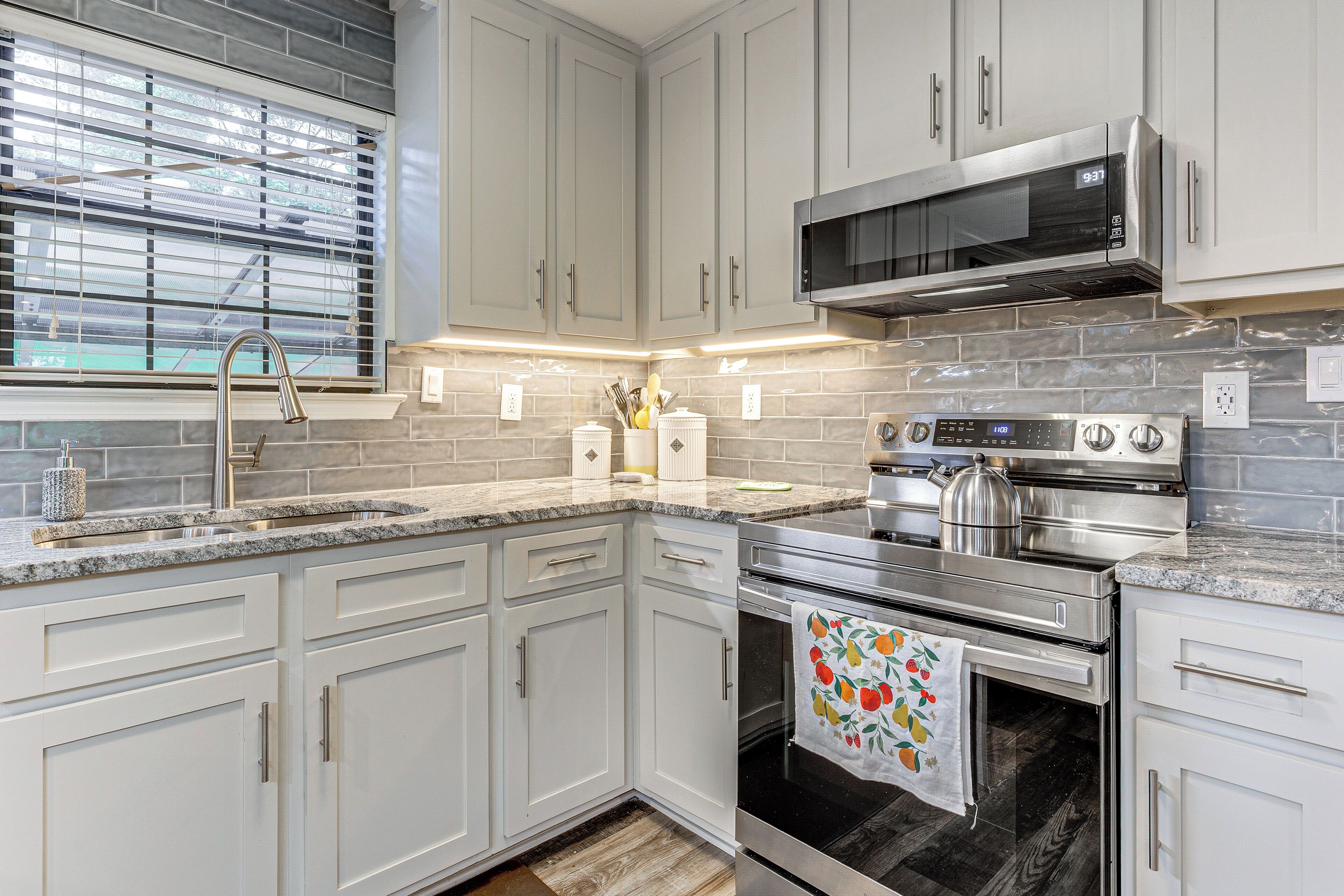 A modern kitchen with white cabinets, a stainless steel range, a microwave, and a window with blinds.