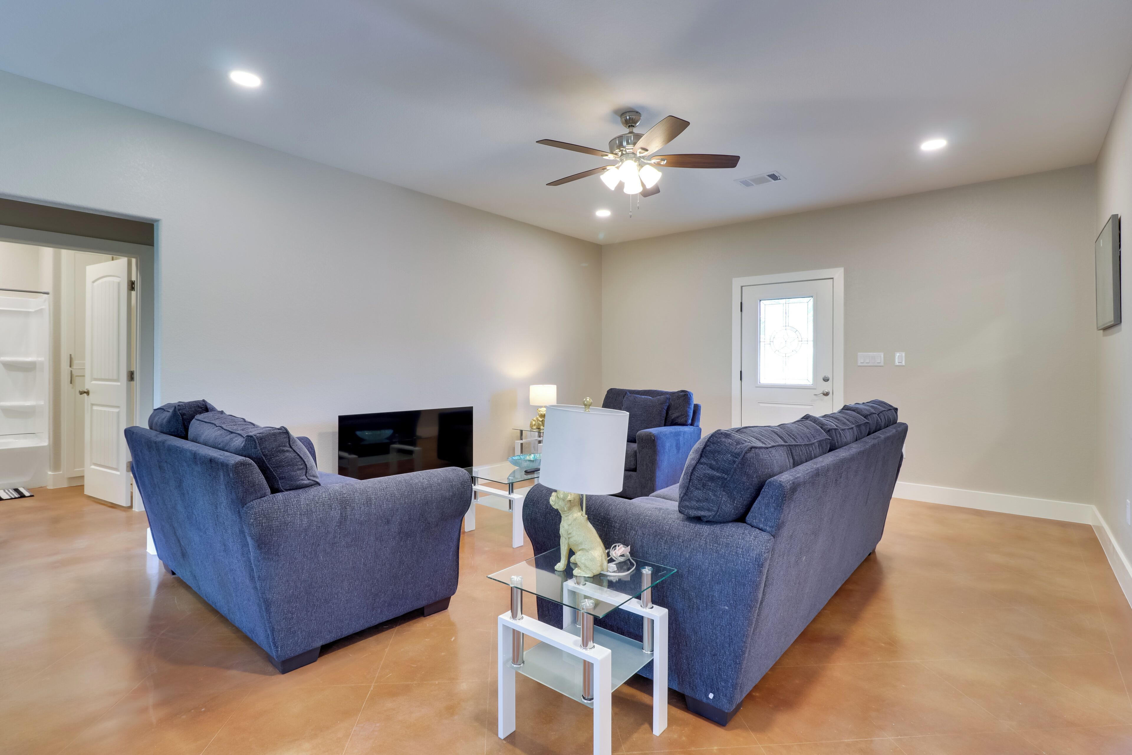 A living room with two grey sofas, a glass coffee table, a ceiling fan, and a TV.