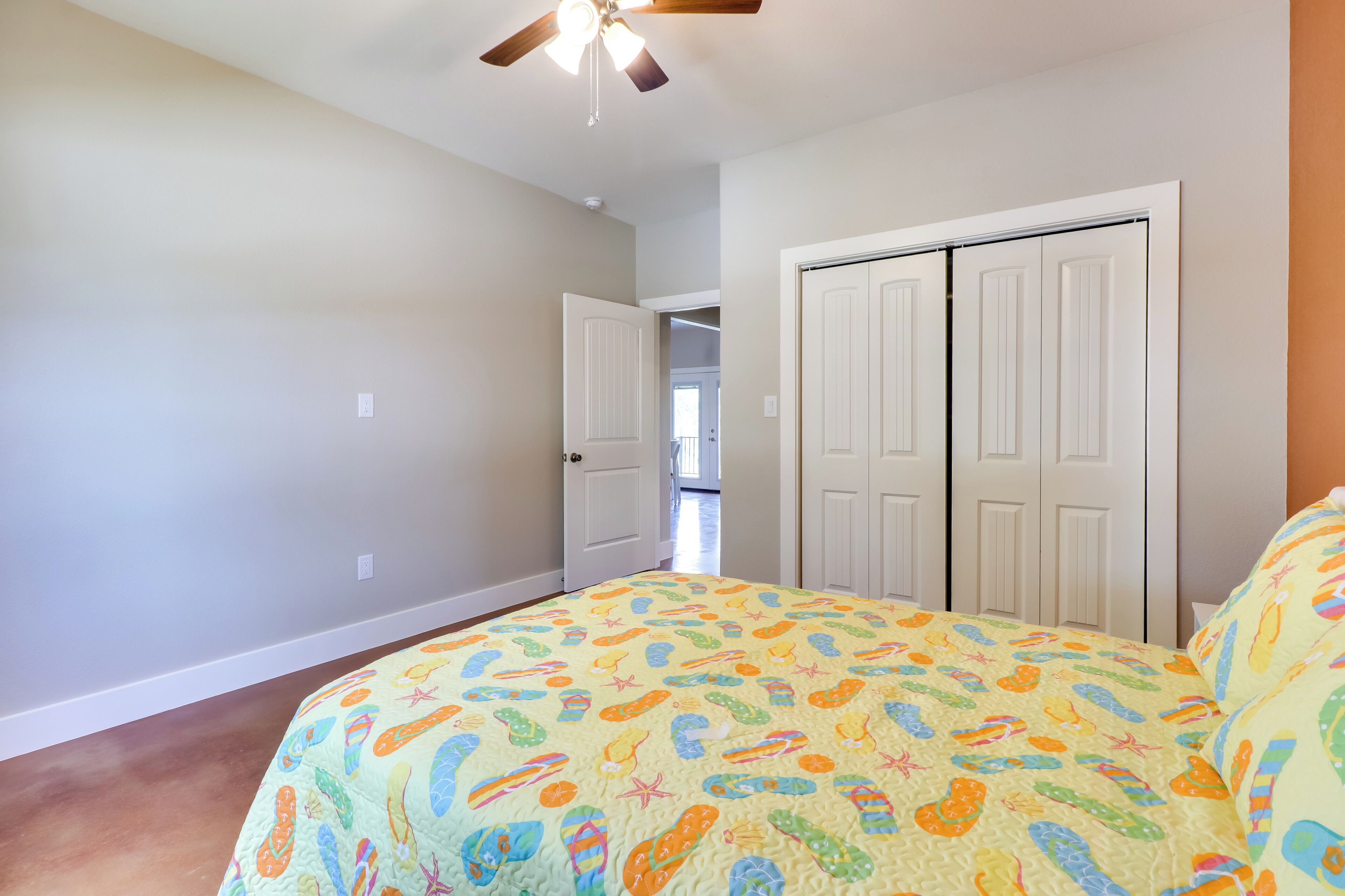 A bedroom with a bed, a ceiling fan, and a door leading to another room.