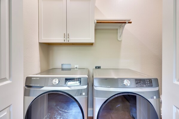 A laundry room with two Samsung washing machines, a white cabinet above, and a small shelf. - 1 Mi to Lake Lbj: Peaceful Home w/ Patio & Yard! (Marble Falls)