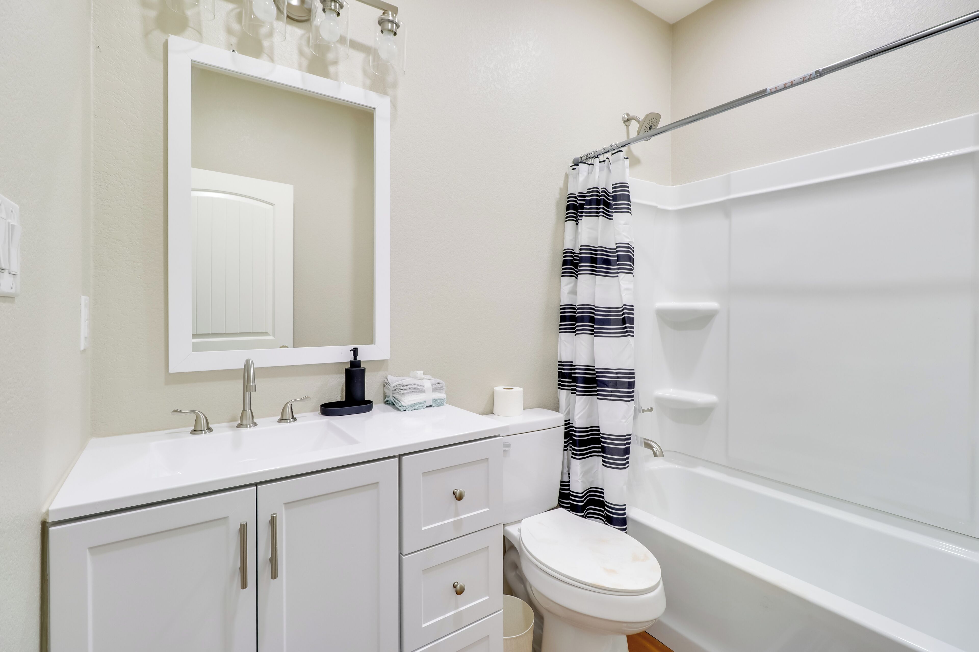 A bathroom with a white sink, mirror, and toilet. There is a striped shower curtain and a white bathtub.