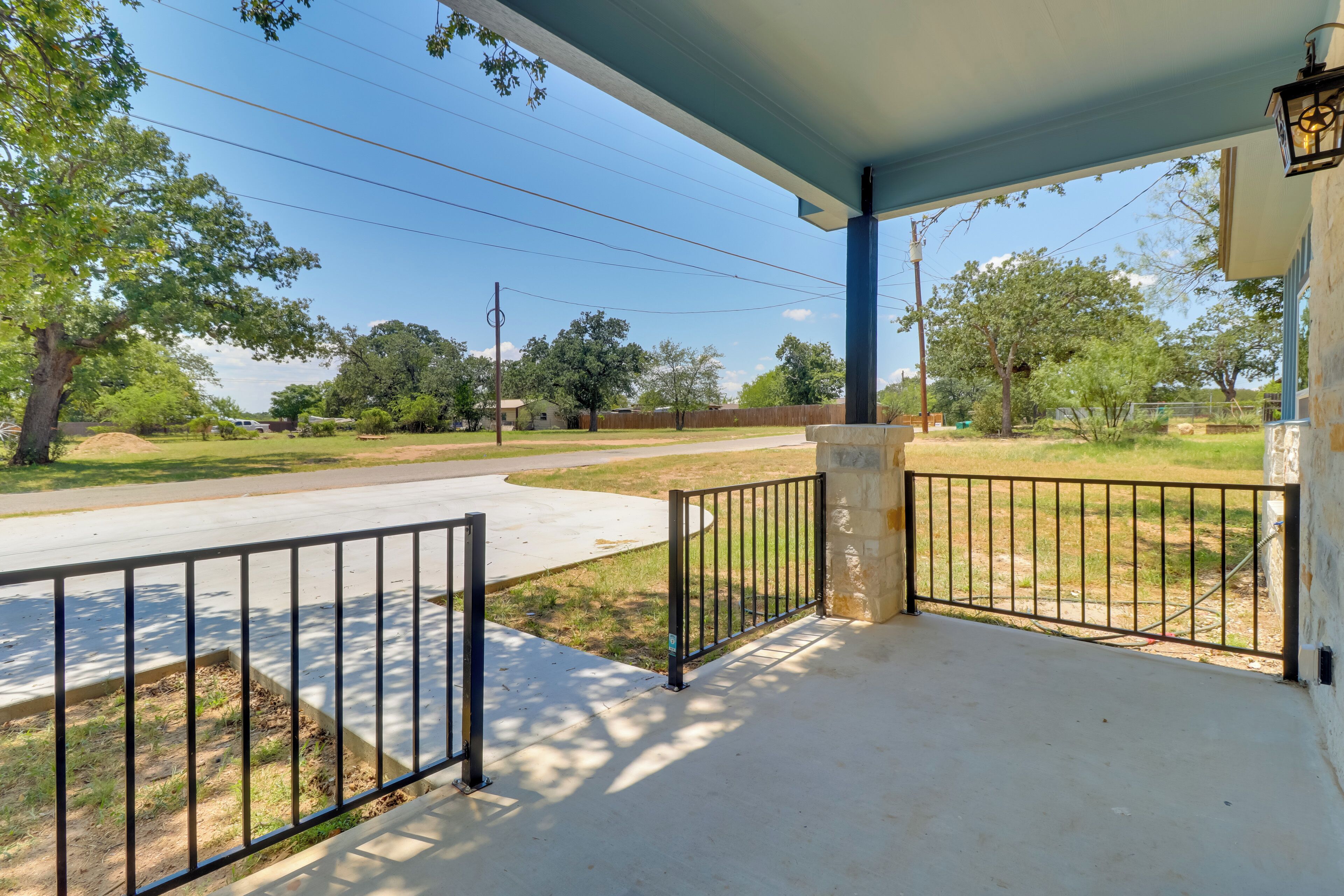 A covered porch with a concrete floor, metal railing, and a stone pillar.
