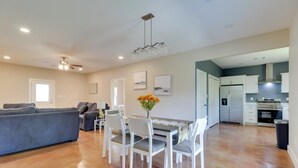 A spacious living area with a gray sofa, dining table with chairs, a ceiling fan, and a kitchen with white cabinets and appliances. - 1 Mi to Lake Lbj: Peaceful Home w/ Patio & Yard! (Marble Falls)