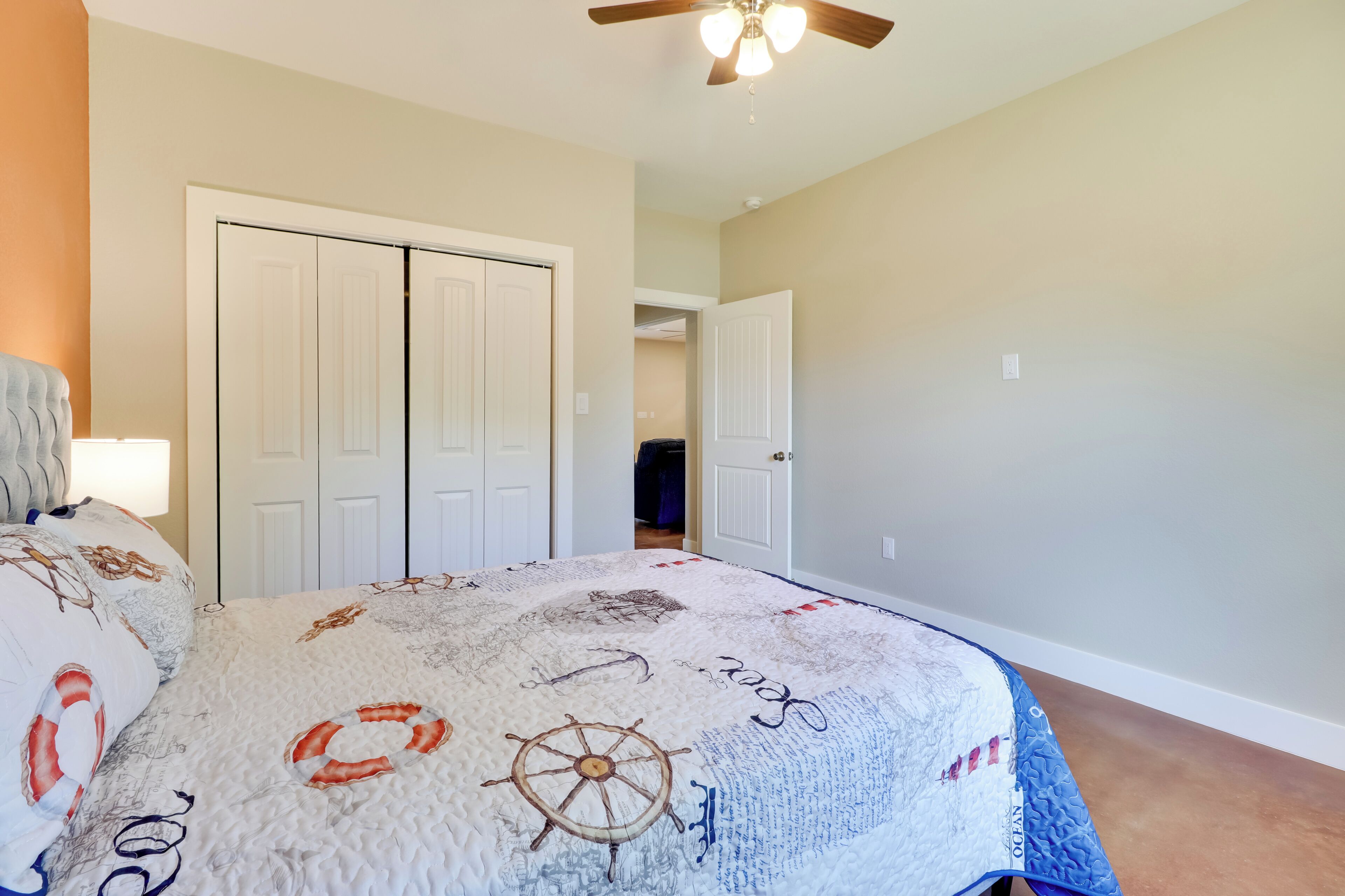 A bedroom with a bed featuring a nautical-themed duvet, a ceiling fan, and a wardrobe with two doors.