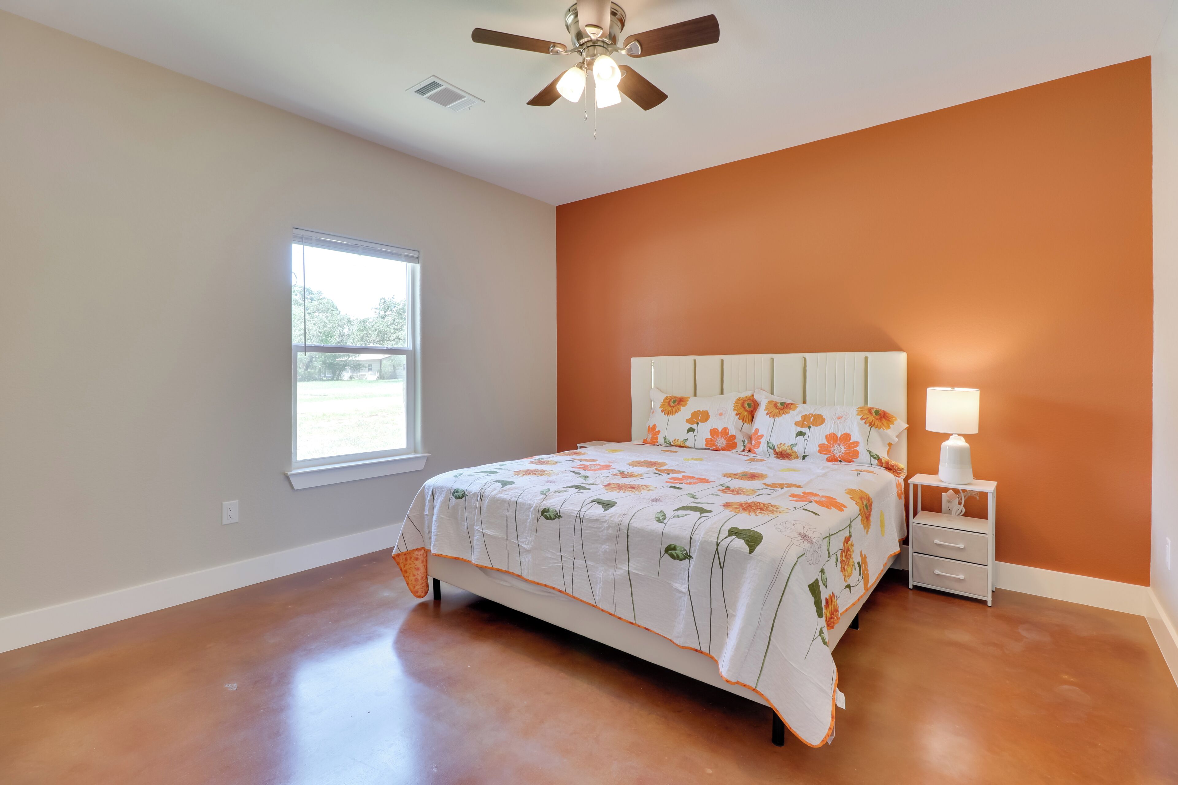 A bedroom with a bed, a nightstand, a ceiling fan, a window, and an orange wall.