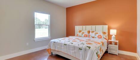 A bedroom with a bed, a nightstand, a ceiling fan, a window, and an orange wall.