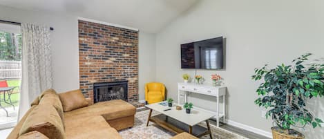 A living room with a brick fireplace, a yellow armchair, a white coffee table, and a large potted plant.