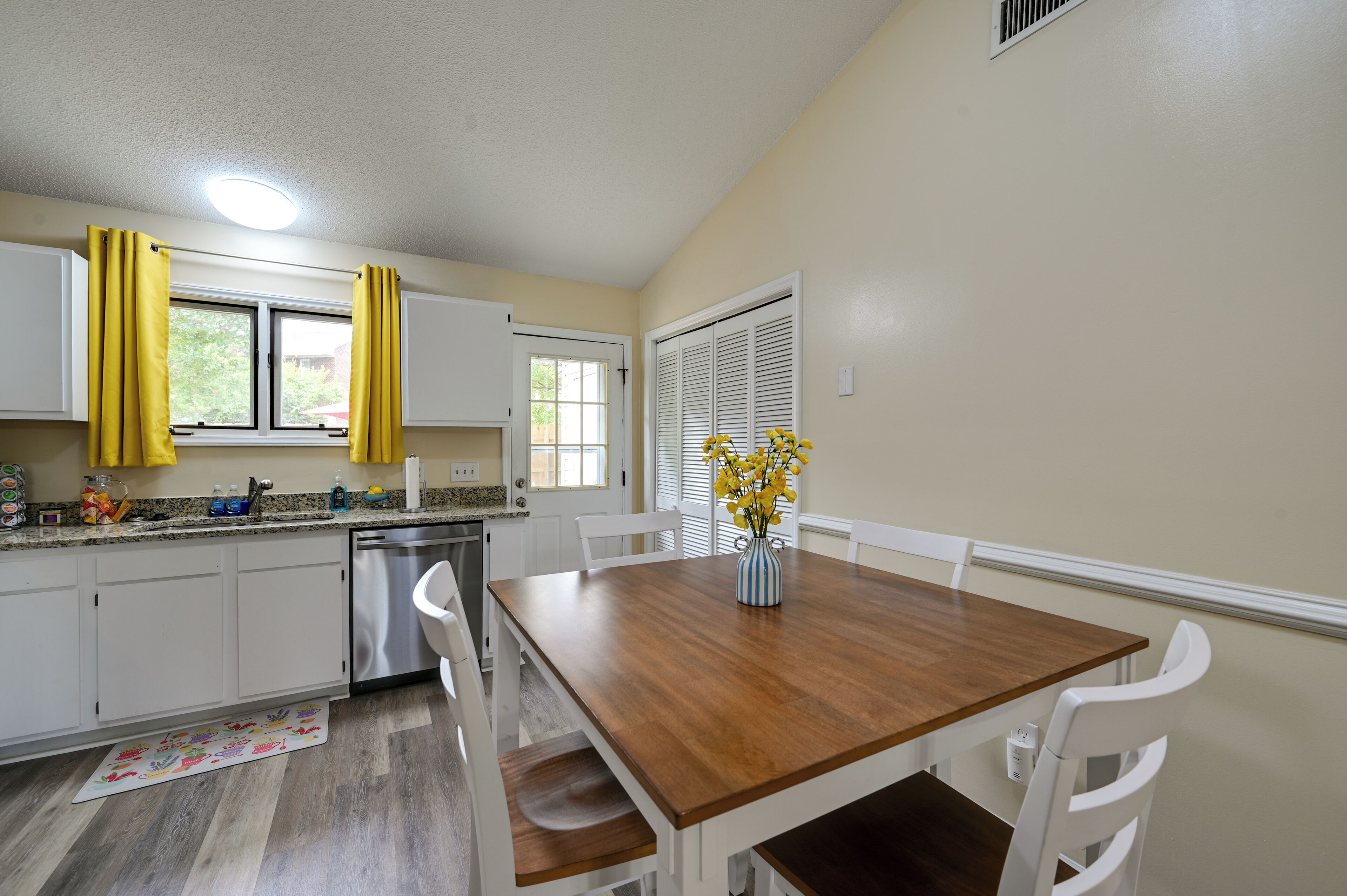 A kitchen with white cabinets, a stainless steel dishwasher, and a wooden dining table with white chairs.