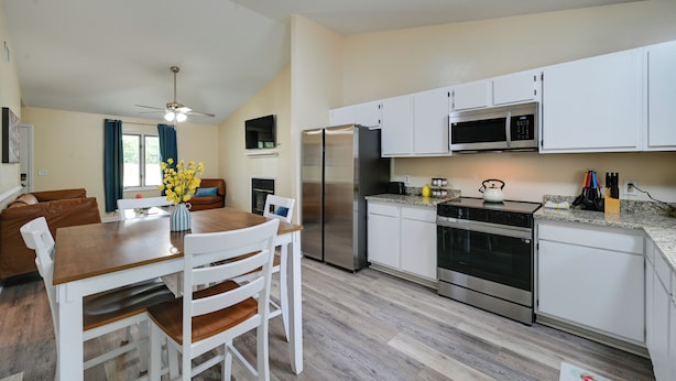 A modern kitchen with white cabinets, stainless steel appliances, and a dining area with a wooden table and white chairs. - Game Day Ready: Greenville Stay w/ Patio Dining (Greenville)