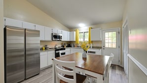 A modern kitchen with white cabinets, stainless steel appliances, and a wooden dining table. - Game Day Ready: Greenville Stay w/ Patio Dining (Greenville)