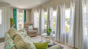 A spacious living room with a beige sofa, a green armchair, and a glass coffee table with a plant. - Tee Off & Soak Up Sun! Airy Englewood Gem w/ Yard (Englewood)