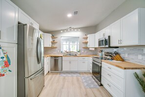 A modern kitchen with white cabinets, stainless steel appliances, and a wooden countertop. - Tee Off & Soak Up Sun! Airy Englewood Gem w/ Yard (Englewood)
