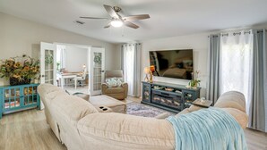 A living room with a sofa, armchair, and a TV. There is a ceiling fan, a fireplace, and a window with curtains. - Tee Off & Soak Up Sun! Airy Englewood Gem w/ Yard (Englewood)