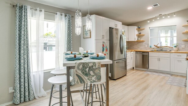 A modern kitchen with white cabinets, a stainless steel refrigerator, and a dining area with a table and bar stools. - Tee Off & Soak Up Sun! Airy Englewood Gem w/ Yard (Englewood)