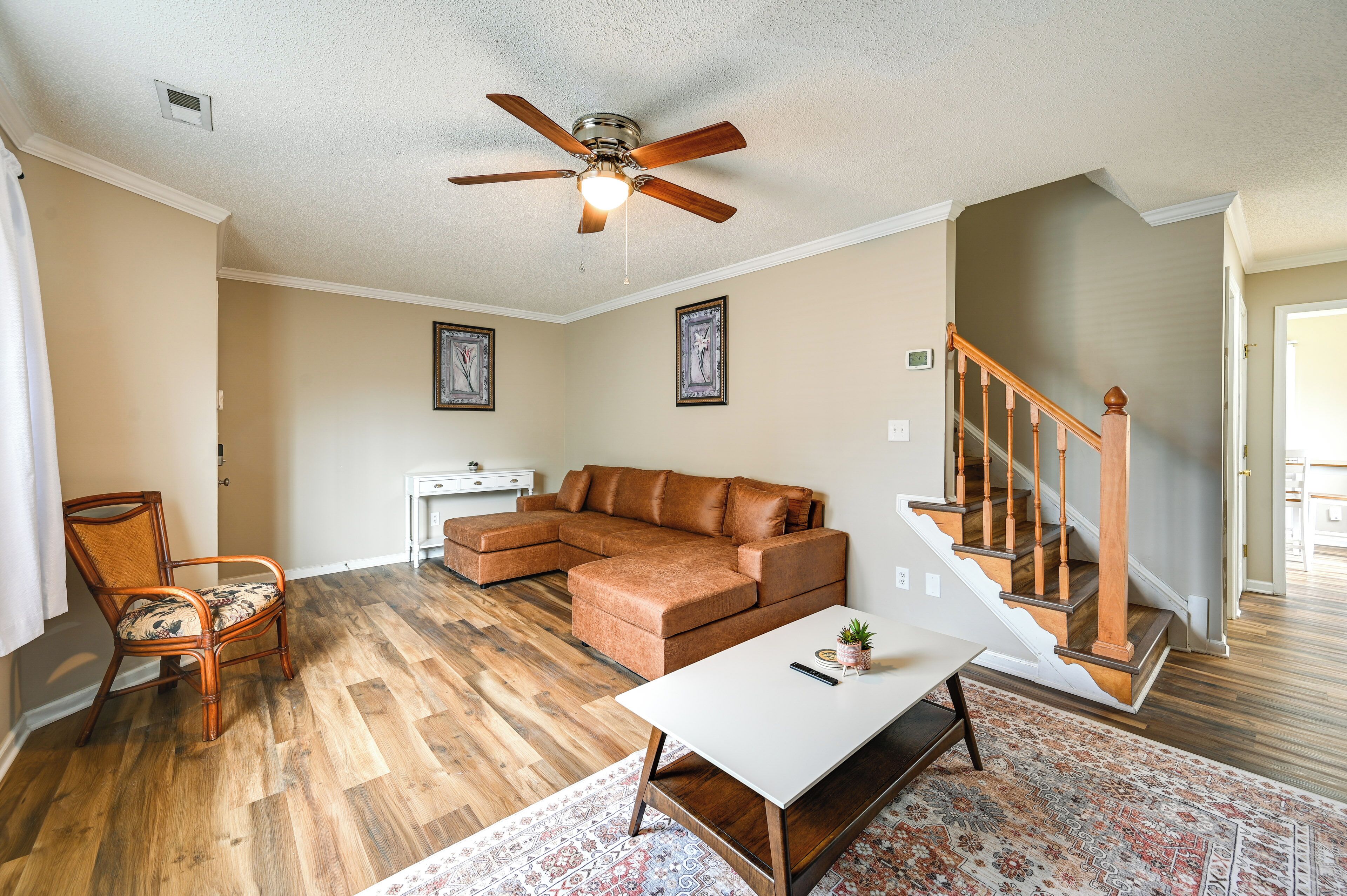 A living room with a sectional sofa, a white coffee table, a wooden floor, a ceiling fan, and a staircase.